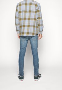 Camisa de franela a cuadros en azul claro, verde y amarillo, combinada con jeans slim-fit azules y zapatillas negras y blancas.