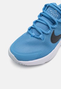 Baskets de course bleu clair avec un dessus texturé, un swoosh noir de Nike et une semelle blanche. Présente un design à lacets et un col rembourré.