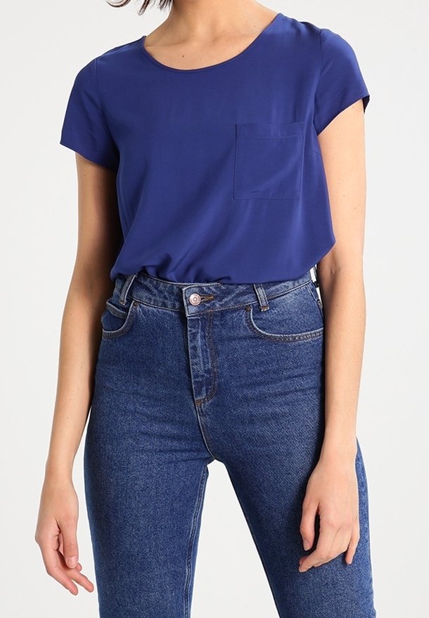 Chemisier bleu marine à manches courtes avec un col rond et un détail de poche, assorti à un jean taille haute bleu, présentant une texture en denim classique.