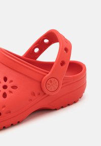 Punane Croslite sabake, millel on reguleeritav kanna rihm, perforatsioon ventilatsiooniks, ringikujuline logo aktsent ja tekstureeritud pind.