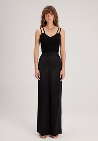 Zwarte geribde tanktop met dunne bandjes, gecombineerd met hoge taille, wijde zwarte broek. Glad textuur met een getailleerd silhouet.