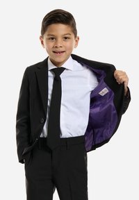 Traje negro con una camisa blanca y corbata negra. La chaqueta está desabrochada, revelando un forro interior púrpura. Ajuste elegante y a medida.