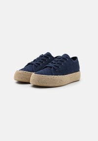 Scarpe da ginnastica in canvas blu navy con motivi in rilievo, dotate di suola in corda di juta e lacci piatti, evidenziando un design informale e un contrasto di texture.