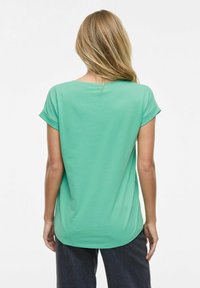 Mintgrön t-shirt med kort ärm, mjukt tyg, rundad nederkant, avslappnad passform, med uppvikta ärmslut och en slät yta. Visad från baksidan.