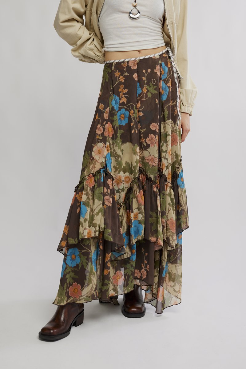 Maksi suknja s višeslojnim naborima, smeđa baza, cvjetni uzorak u plavoj i ružičastoj boji, lepršavi prozirni materijal, uparena sa smeđim gležnjačama.