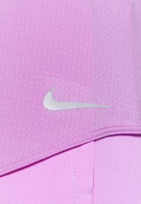 Zbliżenie na fioletową tkaninę z wyszywanym wykończeniem i srebrnym logo Nike w kształcie swoosha na strukturalnym materiale sportowym.