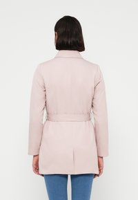 Ροζ ανοιχτό παλτό με ζώνη στη μέση, μακριά μανίκια και γιακά με εγκοπή. Ομαλή υφή, μήκος έως το γόνατο, με αεραγωγό στην πλάτη.