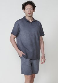 Polo shirt gris foncé en tissu texturé et à manches courtes, associé à un short assorti. La chemise comporte un col subtil et un détail de logo.