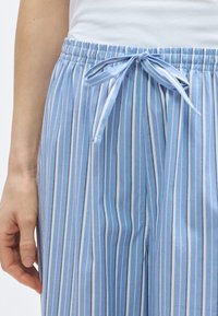 Pantalon de pyjama bleu clair avec rayures blanches verticales, doté d'une ceinture élastique et d'un détail à nouer à l'avant. Texture en coton lisse.