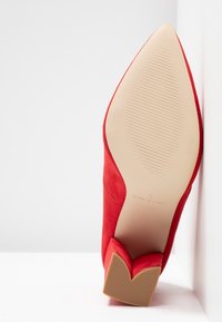 Rote Wildlederschuhe mit hohen Absätzen und spitzem Zehenbereich. Mit einem V-förmigen Design der Absatzbasis.