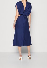 Marinblå midi-klänning med djup rygg, korta ärmar och en figursydd midja. Slätt tyg och subtil drapering ger struktur.
