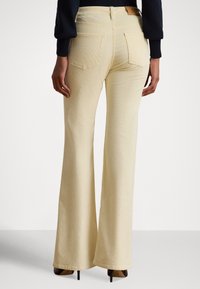 Dzwony wykonane z teksturowanej, jasnobeżowej tkaniny, z wysokim stanem, czterema kieszeniami i tkana etykietą na tylnej części pasa.