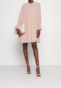 Różowa kwiecista sukienka z długimi rękawami, okrągłym dekoltem i warstwową spódnicą. Połączona z beżową kopertówką i cielistymi sandałami na obcasie z paskami.