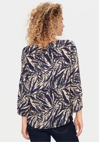 Bluzka w kwiatowy wzór w odcieniach granatu, kremu i niebieskiego, z luźnym krojem, rękawami o długości trzech czwartych oraz teksturowanym materiałem. Widok z tyłu.