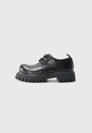 Black leather shoe with a rounded toe, lace-up design, and a thick, serrated black rubber sole. Smooth texture, minimal accents.