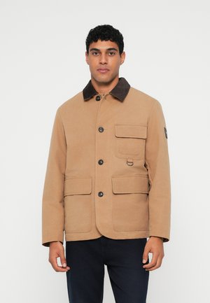 Sandfarvet bomuldsjakke med krave i brunt kordfløj, fire forlommer og knaplukning. Glat tekstur med diskrete syede detaljer.