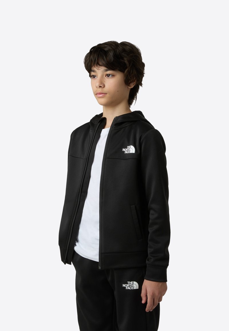 Čierna mikina na zips s hladkým povrchom, s bielym logom na ľavej strane hrude a dvoma prednými vreckami. Nosená cez biele tričko.