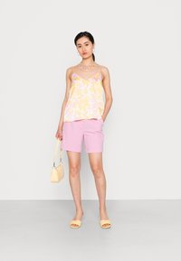 Top sem mangas em amarelo e rosa floral, combinado com calções rosa. Sandálias amarelas e uma pequena bolsa amarela completam o look.