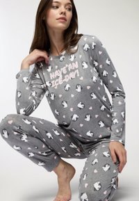 Set di pigiama grigio realizzato in tessuto morbido con un motivo di pinguini e dettagli rosa a forma di cuore, con la scritta "HAVE AN ICE DAY!" stampata in bianco.