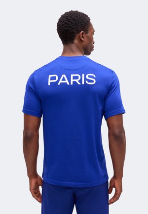 Homme portant un T-shirt bleu avec l'inscription « PARIS » en blanc dans le dos, debout dos à la caméra.