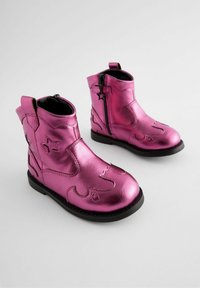 Rosa metallische Stiefeletten mit glänzender Oberfläche, ausgestattet mit einem Reißverschluss, dekorativen Nähten und Sternakzenten an der Seite. Schwarze Gummisohle.