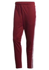 Maroon athletic pants with an elastic waistband, featuring two vertical white stripes along the sides, smooth texture, and tapered design.