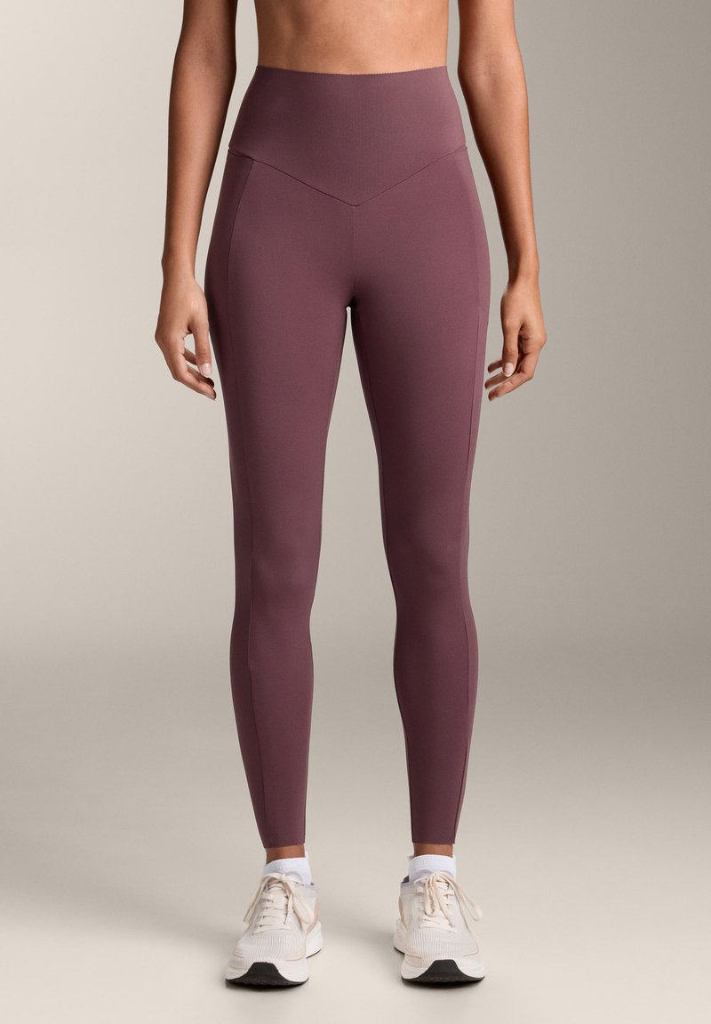 Vysoké legíny v tmavej purpurovej farbe, vyrobené z hladkého, elastického materiálu. Majú bezšvový dizajn a priliehavý strih, skombinované so bielymi športovými topánkami.