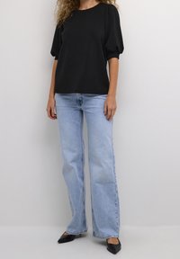 Svart topp med puffärmar, i kombination med ljusblå raka jeans och svarta spetsiga klackar. Slät tyg med en avslappnad passform.