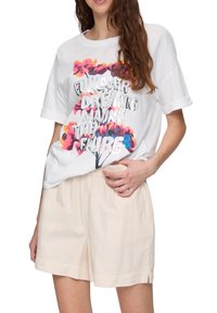 Witte t-shirt met korte mouwen, voorzien van een kleurrijke bloemenafbeelding en tekst, gecombineerd met lichtbeige gestreepte shorts. Losse pasvorm, zachte stof.