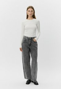 Bela majica s dolgimi rokavi, siva široka kavbojka z sprednjimi žepi in detajli šivanja, v kombinaciji z črnimi čevlji. Preprost, sodoben dizajn.