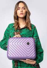 Maleta morada con un diseño texturizado y estriado y un logo de diamante. Presenta un exterior duradero y un asa resistente para llevar.