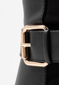Black leather belt featuring a gold-tone metal buckle, with a smooth texture and contrast stitching detail along the edges.