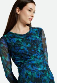 Langärmliges Kleid mit einem bunten blauen und grünen abstrakten Muster auf schwarzem Hintergrund. Es besteht aus glattem Stoff und hat eine figurbetonte Silhouette.