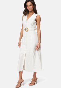 Robe midi en lin blanc avec un décolleté en V, sans manches, et une large ceinture avec boucle ronde, agrémentée d'un fente à l'avant.