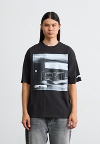 Sort t-shirt med et stort grafisk tryk af racing-elementer, herunder teksten "FORMULA 1" og "P1", med en afslappet pasform og korte ærmer.
