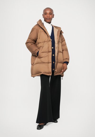 Casaco puffer castanho com textura acolchoada, capuz e bolsos laterais. Combinado com um cardigã azul-marinho e calças flare pretas.