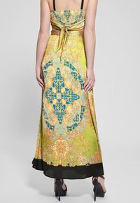 Lang, gele satijnen jurk met ornamentele blauwe en gouden patronen; heeft een gerimpelde lijfje en een zwarte zoom. Vastgebonden aan de achterkant. Hakken zichtbaar.