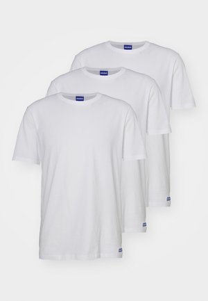 Tres camisetas de algodón blancas con cuello redondo, mangas cortas y etiquetas de logo azul cerca del dobladillo. Textura suave y corte estándar.