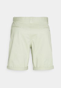Pantaloni corti verde chiaro realizzati in un tessuto con una texture liscia. Presentano risvolti, una chiusura con bottone e due tasche posteriori.