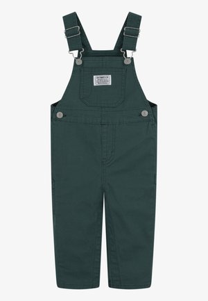 Salopette in cotone verde scuro con spalline regolabili, ganci metallici, tasca anteriore a toppa e dettaglio con bottoni sui lati. Tessuto liscio e gamba dritta.