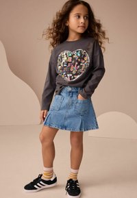 Grå långärmad t-shirt med ett hjärtformat paljettdesign, ihopparad med en ljusblå denimkjol och svarta sneakers med vita detaljer.