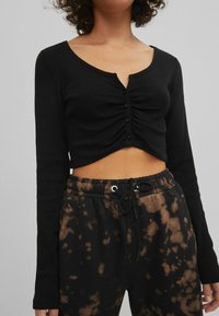 Černý žebrovaný crop top s dlouhým rukávem, výstřihem do V a knoflíkovým detailem, kombinovaný s tmavými tie-dye tepláky s elastickým pasem.