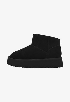 Bottines en suede noir avec une semelle en caoutchouc plate, présentant un bout rond et un design minimaliste. Texture lisse avec une silhouette simple et épurée.