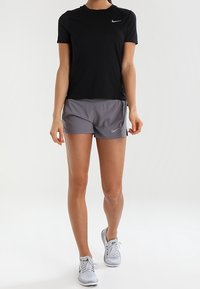 Camiseta atlética negra de manga corta con el logo de Nike, combinada con pantalones cortos atléticos grises, ambos hechos de un tejido ligero y transpirable.