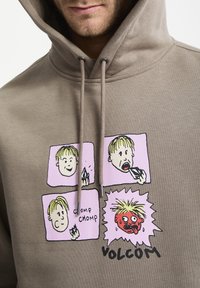 Sudadera marrón con gráficos de dibujos animados en rosa, que muestra cuatro viñetas con personajes divertidos y el texto "VOLCOM". Diseñada con una capucha ajustable.