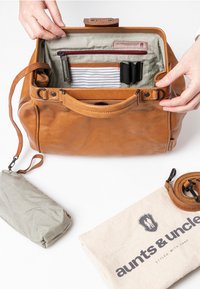 Tan leren handtas met een ritssluiting, binnenzakken en gestreepte voering. Inclusief een groen gestreepte pouch en een afneembare schouderriem.