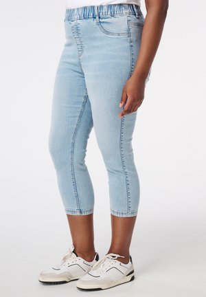 Lichtblauwe stretchdenim capri jeans met een elastische tailleband, met een slim fit en een klassiek vijf-pocket ontwerp. Draagt een paar witte sneakers.