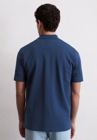 Navyblauwe polo met een gestructureerd ontwerp, korte mouwen en een klassieke kraag, gecombineerd met lichte denim jeans.