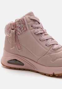 Zapatillas de skate altas rosas con un cuello de punto texturizado, cierre de cordones en la parte frontal y cremallera en el costado. Incluyen una suela con amortiguación visible y suela de goma.