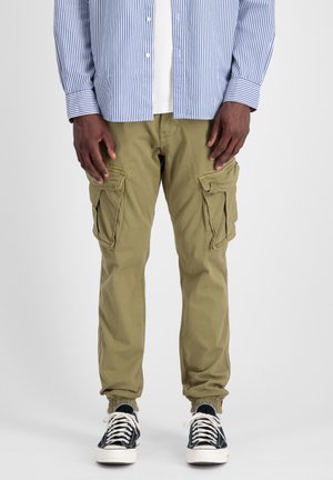 Khaki cargobroek met meerdere zijzakken, elastische boorden en een relaxte pasvorm. Draagt met zwart-witte sneakers. Katoenen materiaal.